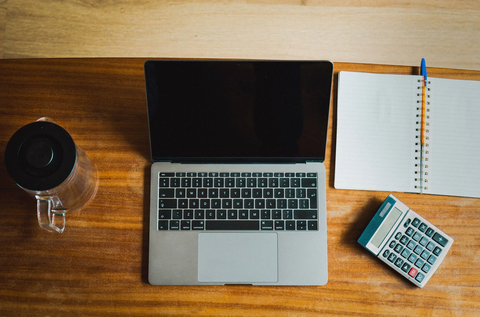 A laptop, notebook and calculator on a desk